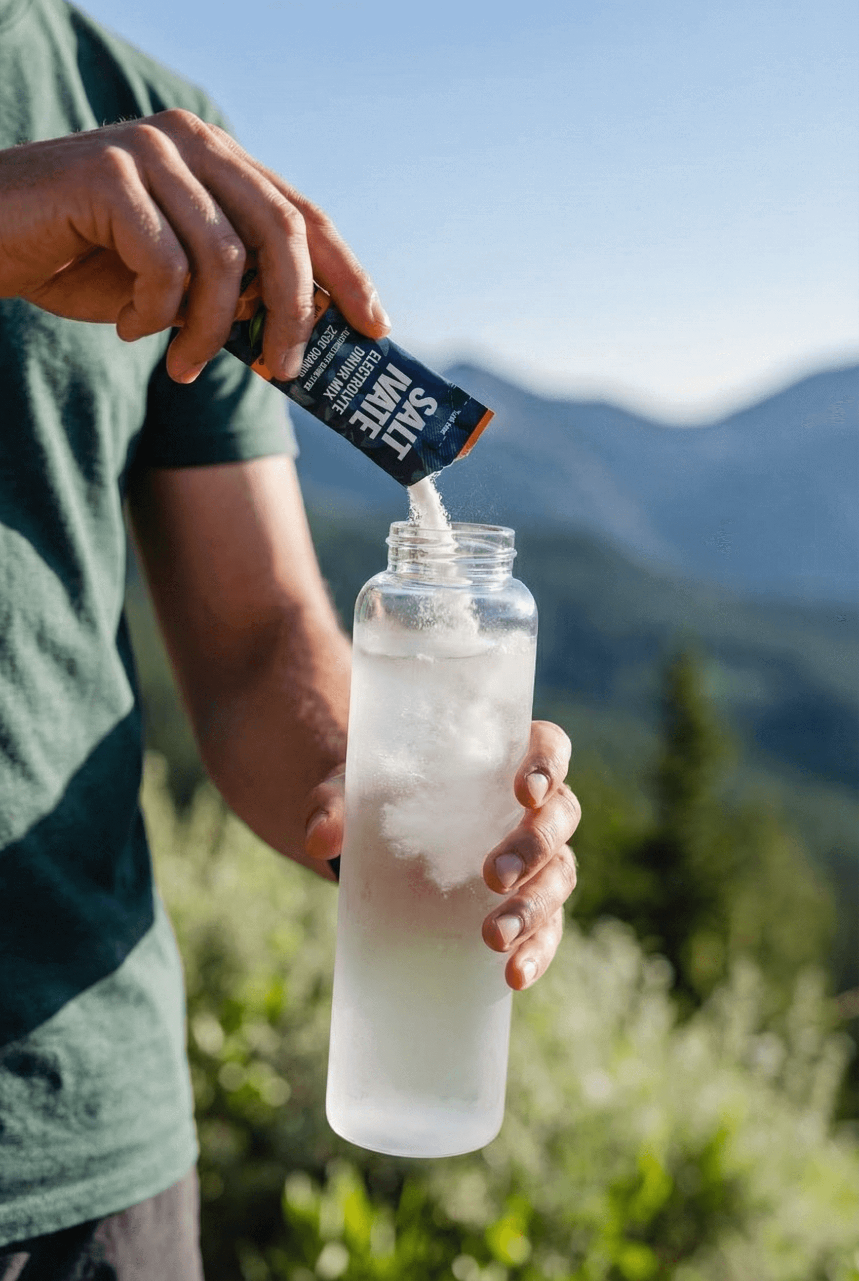 Pouring Saltivate stick pack into water bottle in the mountains