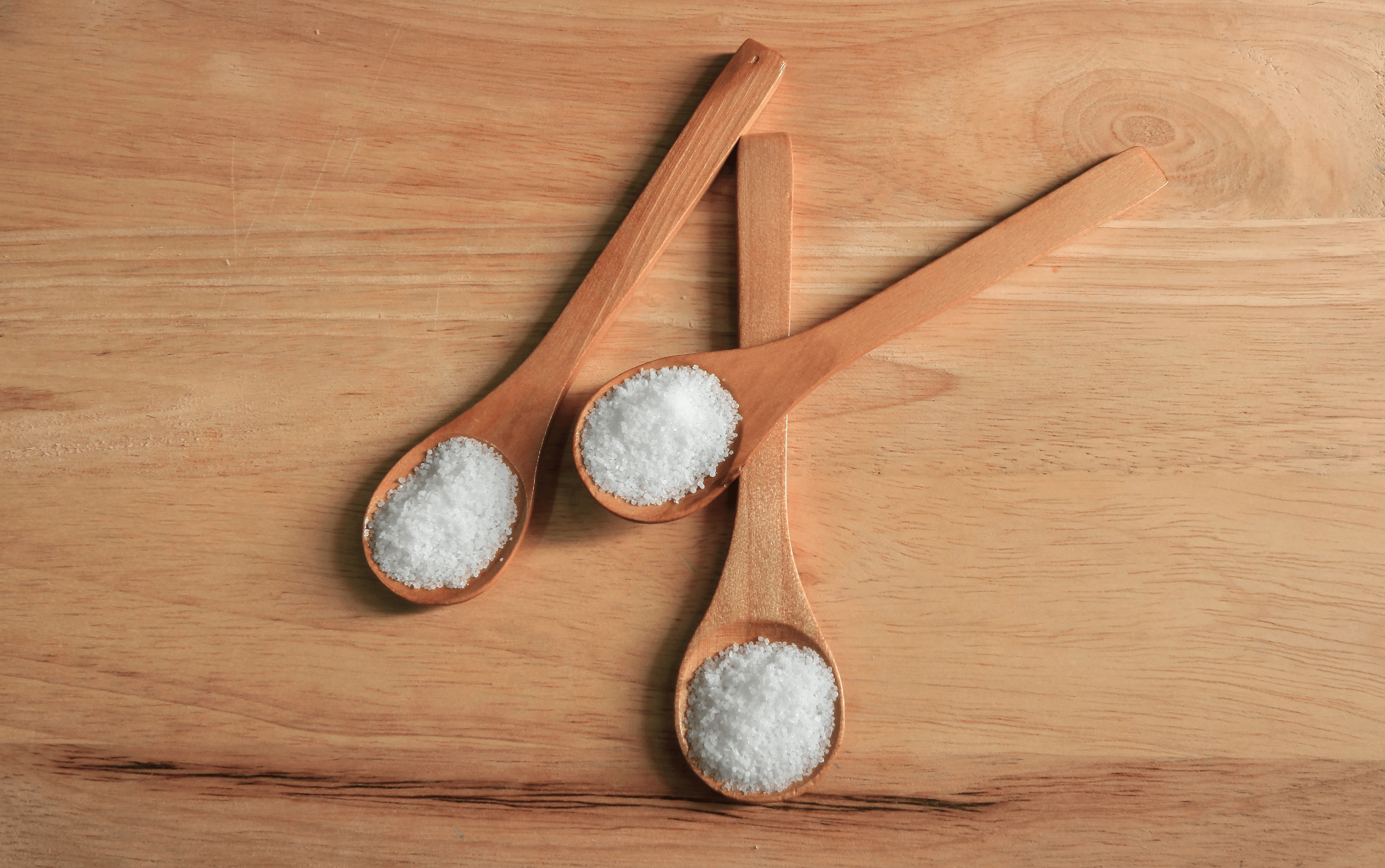 Three wooden spoons filled with salt on a wooden surface
