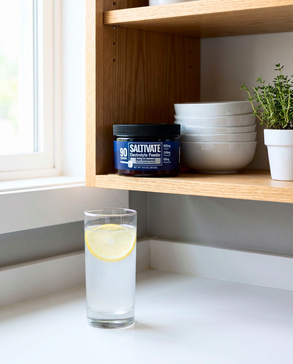 Saltivate Raw Unflavored jar on an oak kitchen shelf, lemon water on the counter below