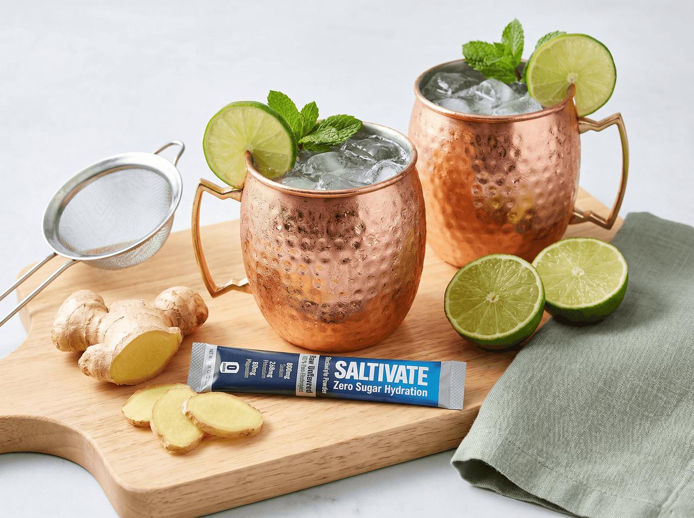 Two copper mugs of ginger mule mocktail with lime, mint, and a Saltivate stick packet
