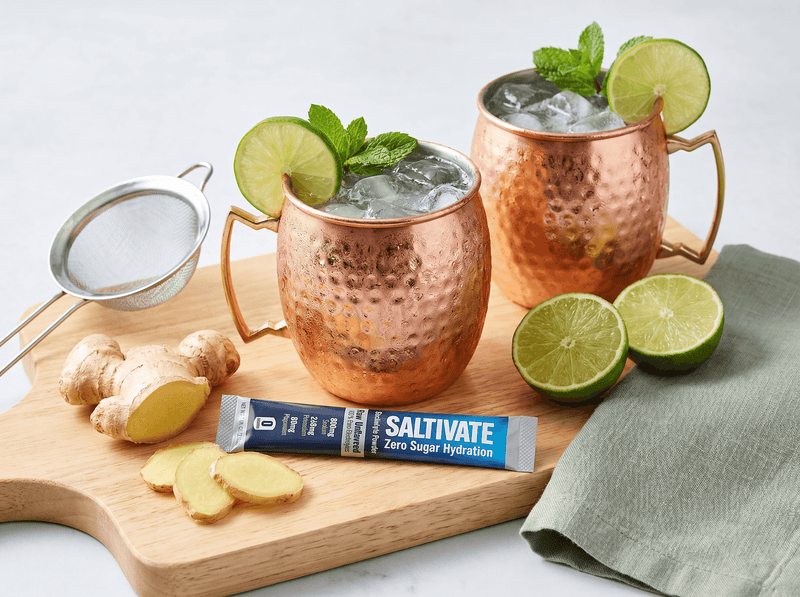 Two copper mugs of ginger mule mocktail with lime, mint, and a Saltivate stick packet