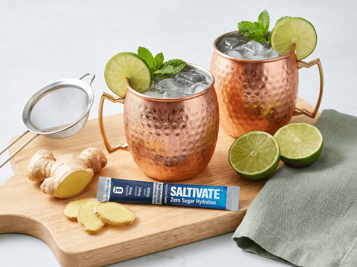 Two copper mugs of ginger mule mocktail with lime, mint, and a Saltivate stick packet