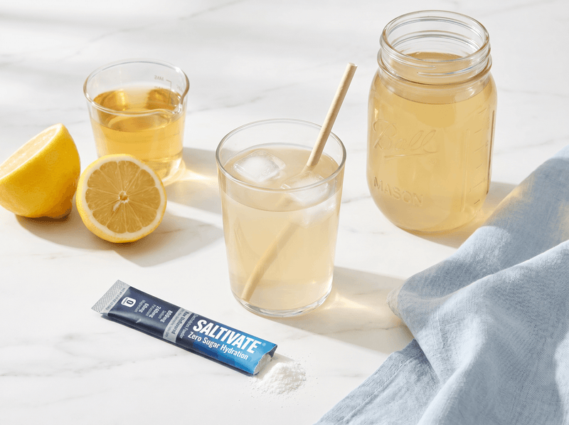 Glass and mason jar of homemade electrolyte drink with a torn Saltivate stick packet