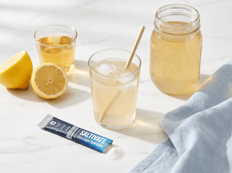 Glass and mason jar of homemade electrolyte drink with a torn Saltivate stick packet