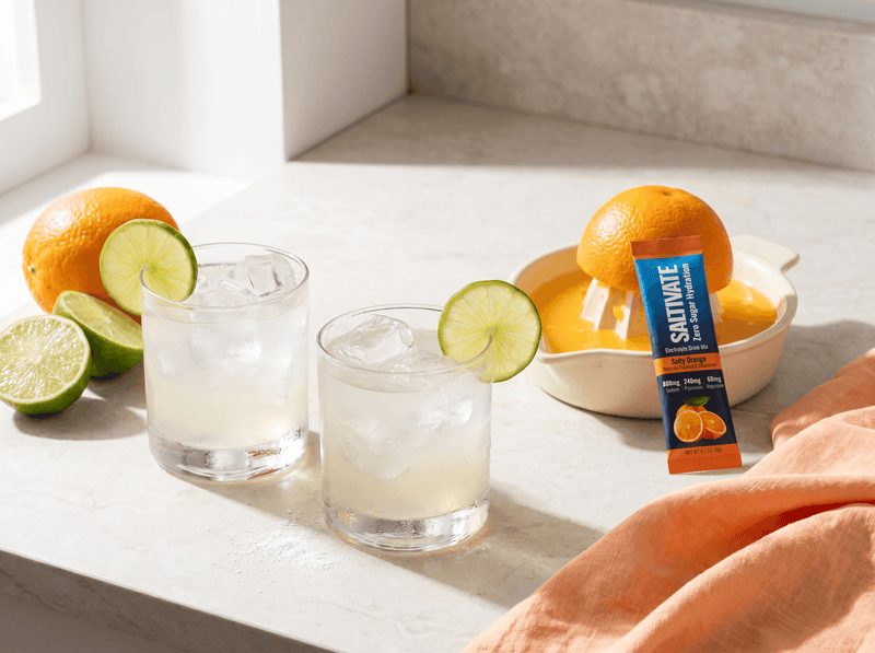 Two salty margarita mocktails with lime wheels and a Saltivate Orange stick packet
