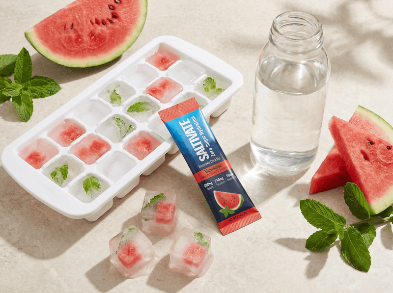 Ice cube tray of clear electrolyte cubes with watermelon chunks and a Saltivate Watermelon stick packet