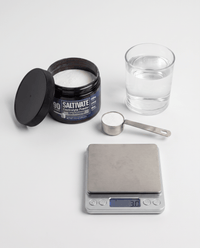 Raw Unflavored jar, level 3 gram scoop, and glass of water on a scale