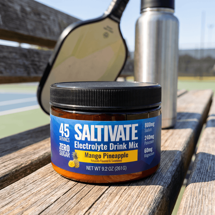Saltivate Mango Pineapple electrolyte jar on a pickleball court bench with a paddle and water bottle
