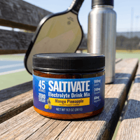 Saltivate Mango Pineapple 45-serving jar courtside on a bench with a pickleball paddle and water bottle
