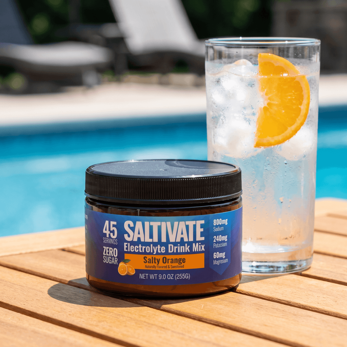 Saltivate Salty Orange 45-serving jar on a poolside table next to a glass of ice water with an orange slice