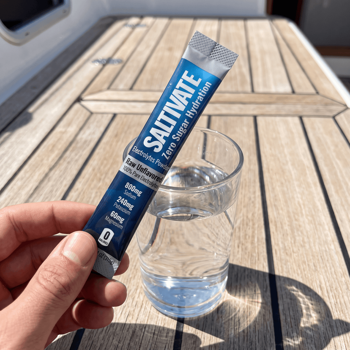Hand holding a Saltivate Raw Unflavored stick over a glass of water on a boat deck