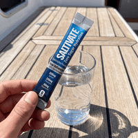 Hand holding a Saltivate Raw Unflavored stick over a glass of water on a boat deck