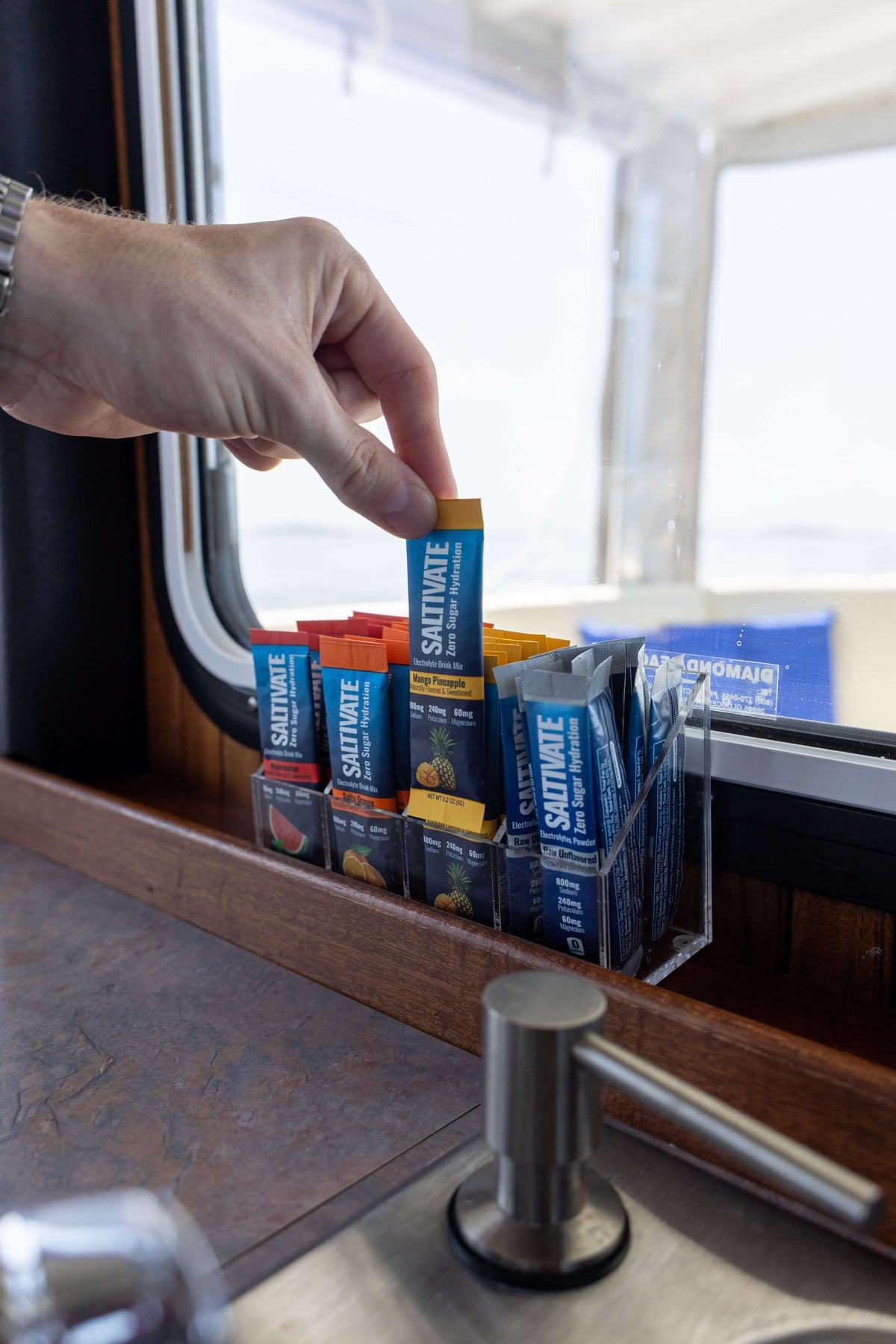 Hand grabbing a Saltivate stick from the acrylic organizer on a boat