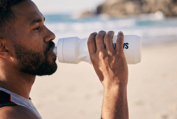 Man drinking from Saltivate bottle on beach