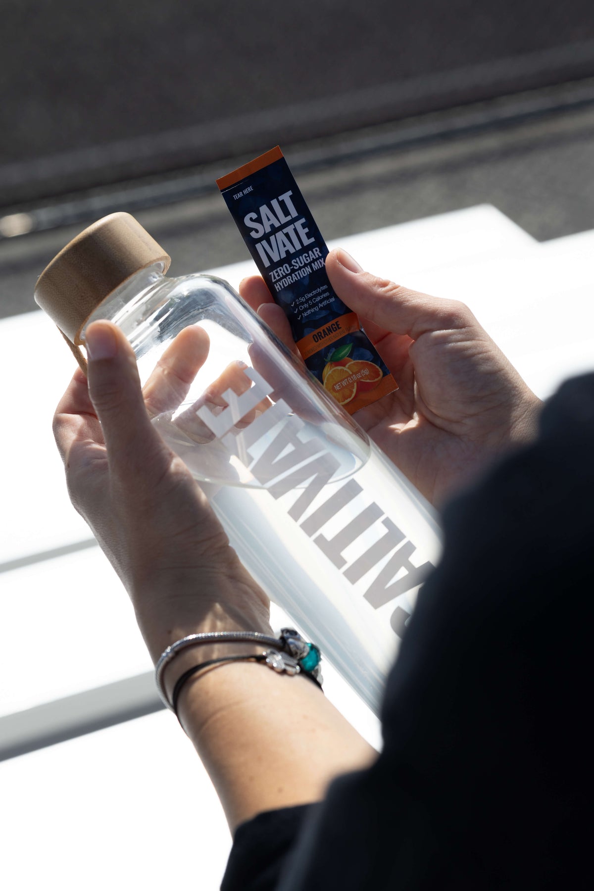 Hands holding a Saltivate glass bottle and an orange stick pack
