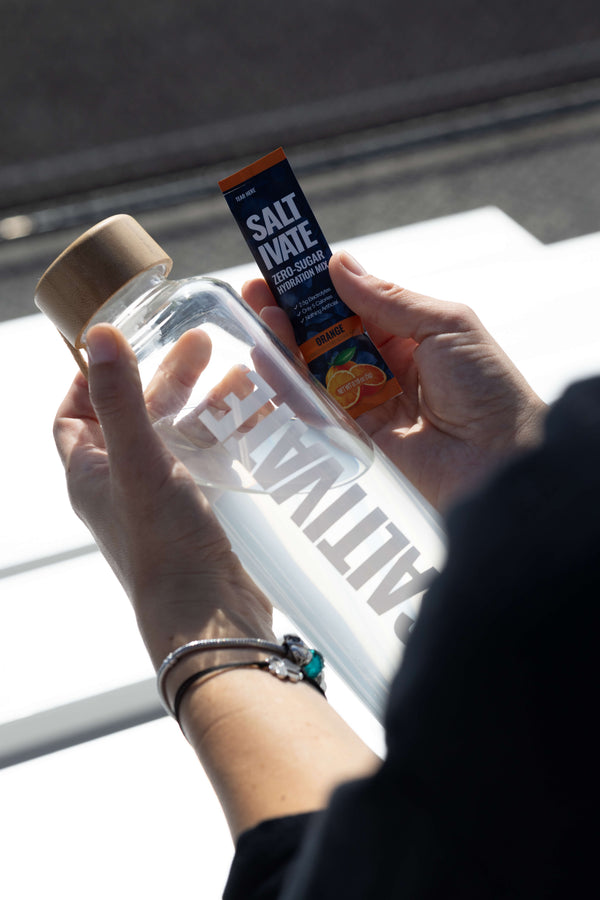 Hands holding a Saltivate glass bottle and an orange stick pack