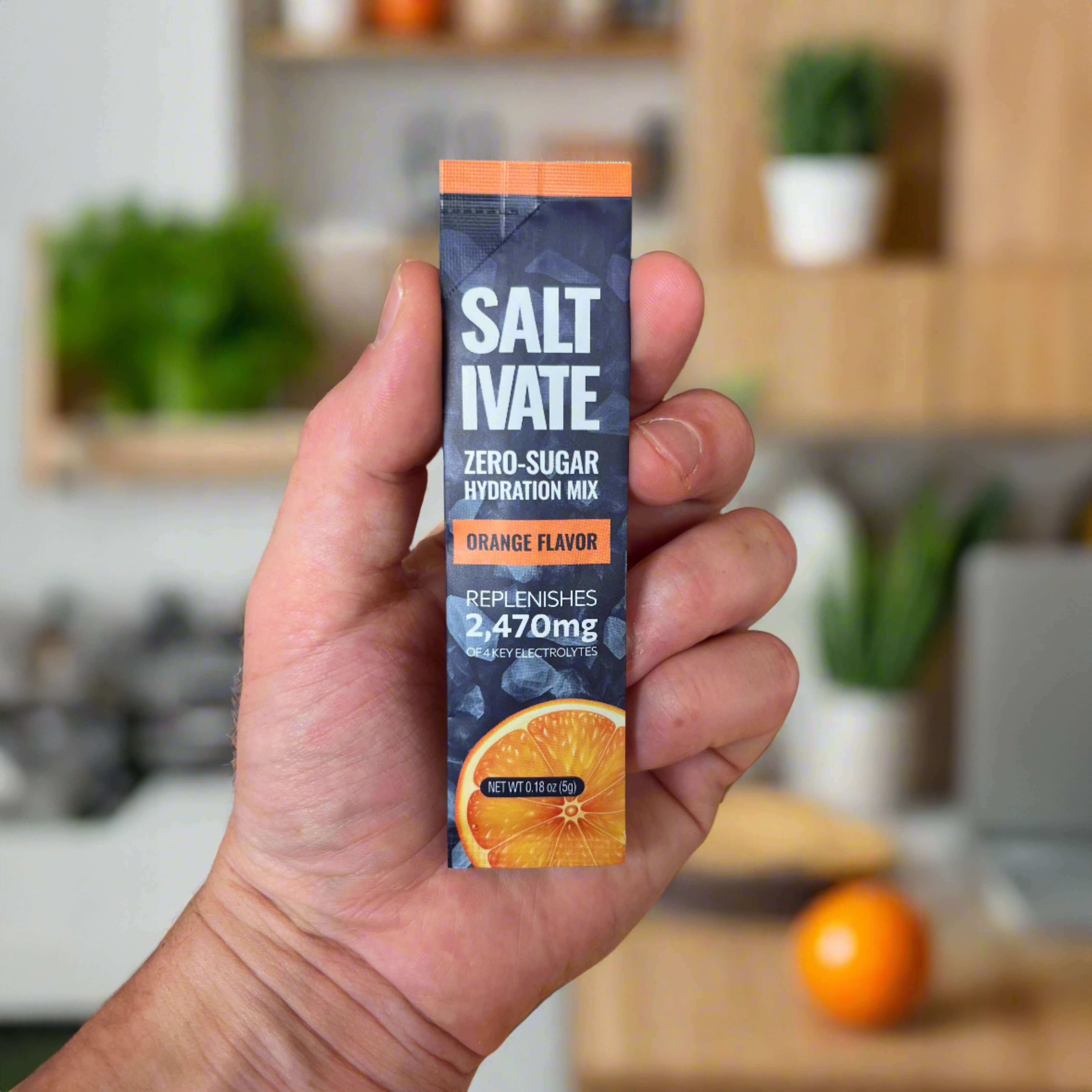 Orange stick packs of Saltivate electrolyte powder in a person's hand, displayed on a kitchen counter with plants in the background.