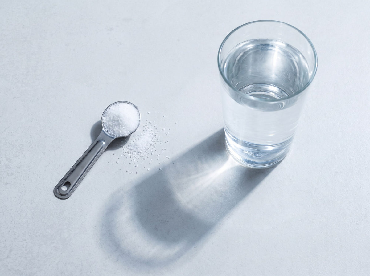 A level measuring teaspoon of table salt next to a glass of clear water