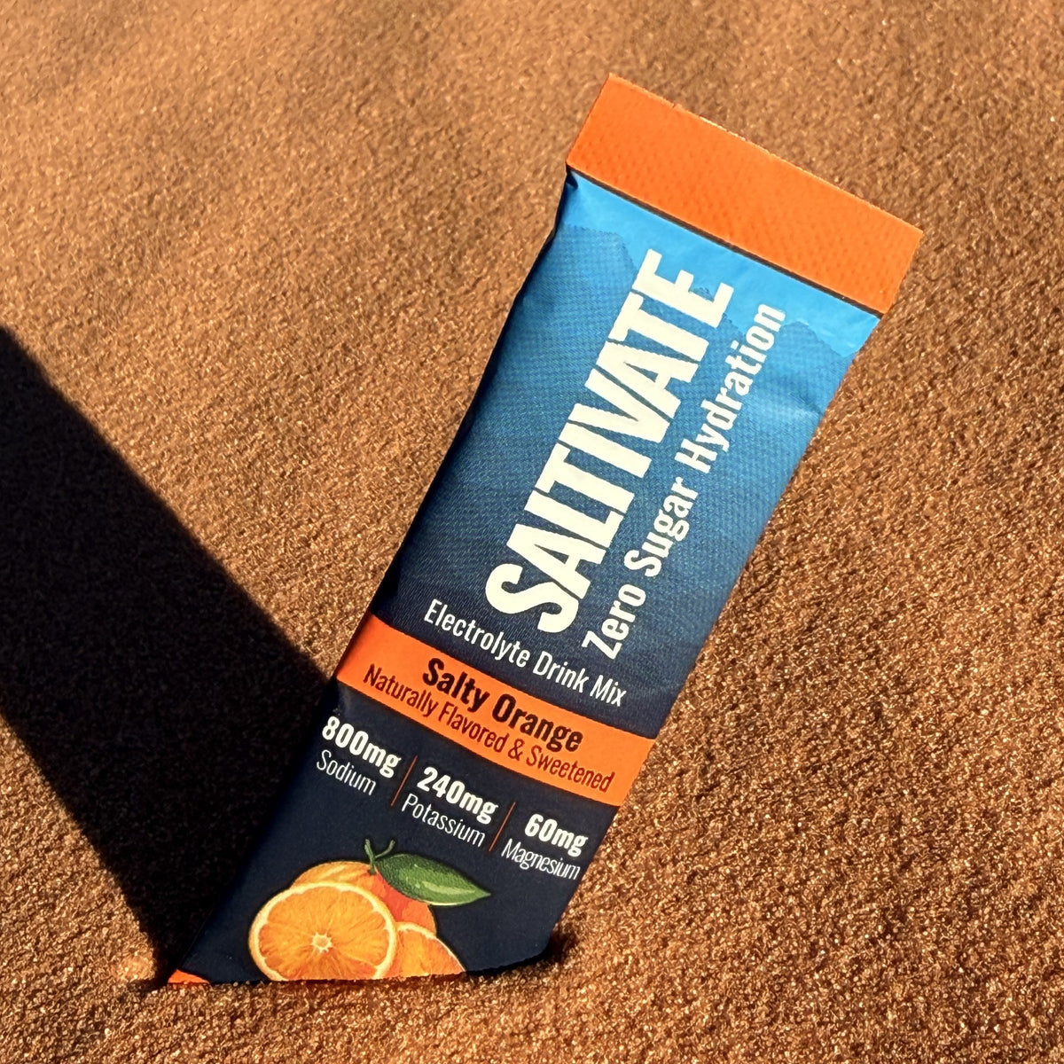Saltivate Salty Orange electrolyte stick standing in rippled orange sand at sunset