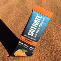 Saltivate Salty Orange electrolyte stick standing in rippled orange sand at sunset