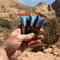 Hand holding Saltivate Watermelon, Mango Pineapple, and Salty Orange sticks in front of Utah sandstone cliffs