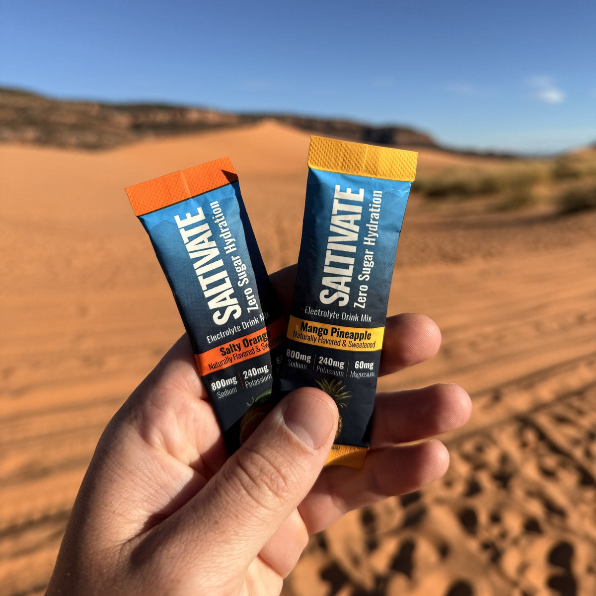 Hand holding Saltivate Salty Orange and Mango Pineapple sticks at the Coral Pink Sand Dunes in Utah