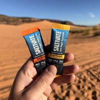 Hand holding Saltivate Salty Orange and Mango Pineapple sticks at the Coral Pink Sand Dunes in Utah
