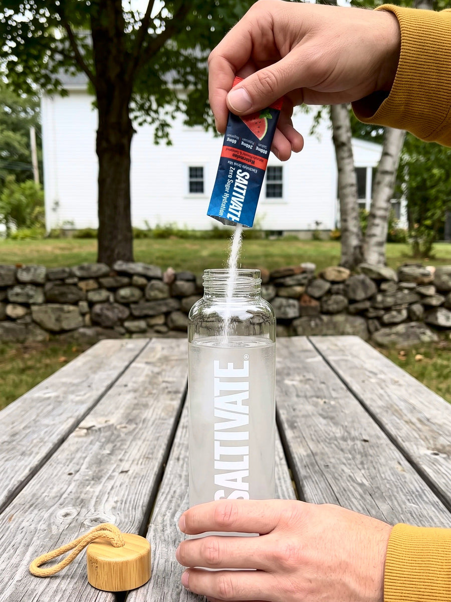 Hands pouring a torn Saltivate Watermelon packet into an open glass bottle of water
