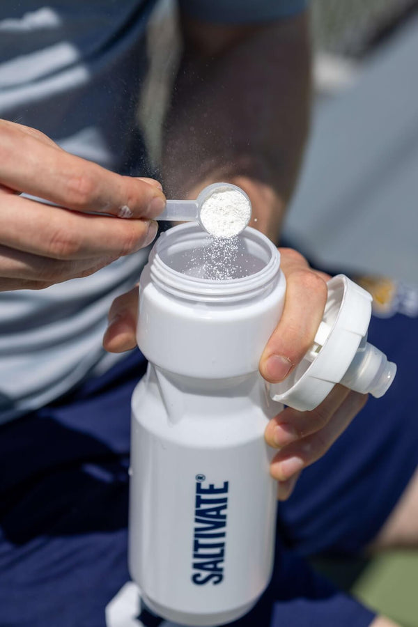 Hands tipping a scoop of powder into a white Saltivate squeeze bottle
