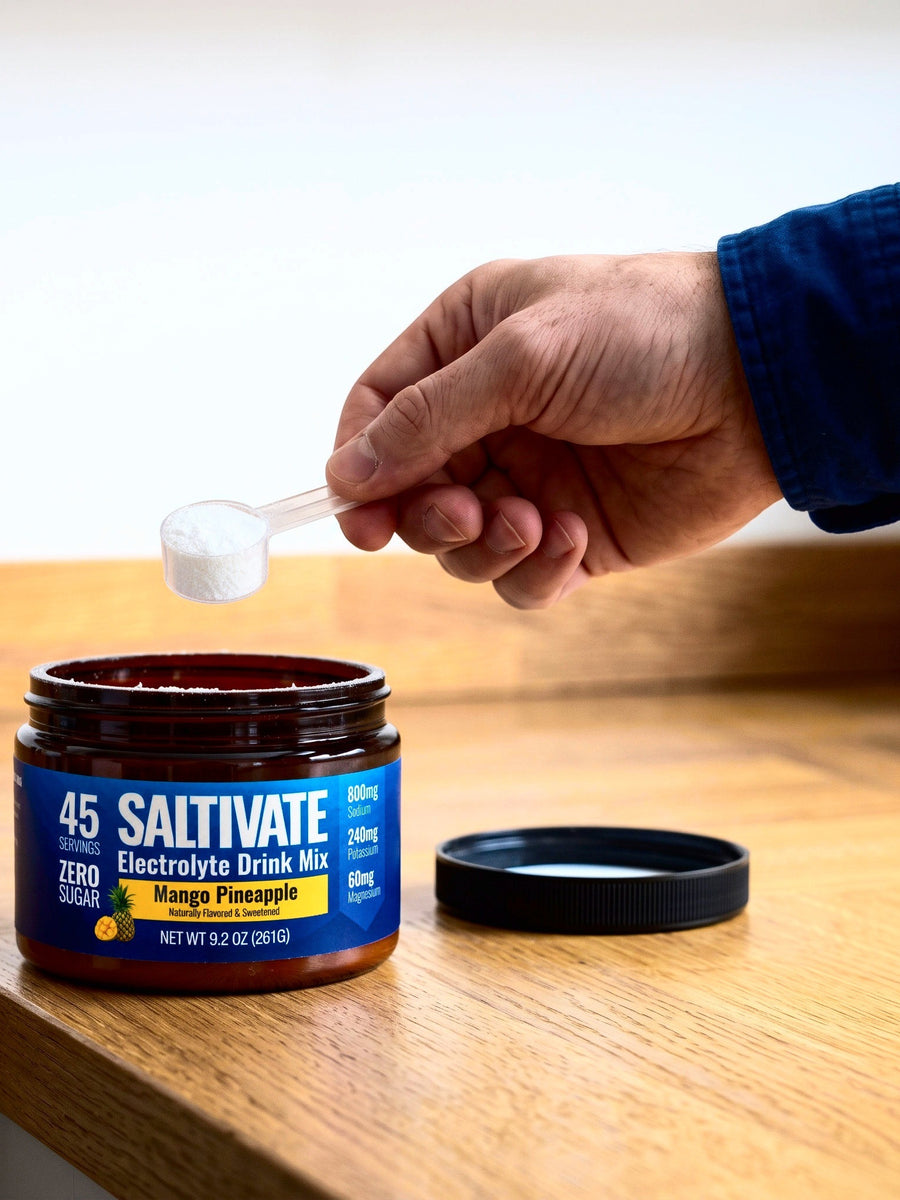 A hand lifting a clear scoop of white powder out of an open Saltivate jar, the black lid beside it